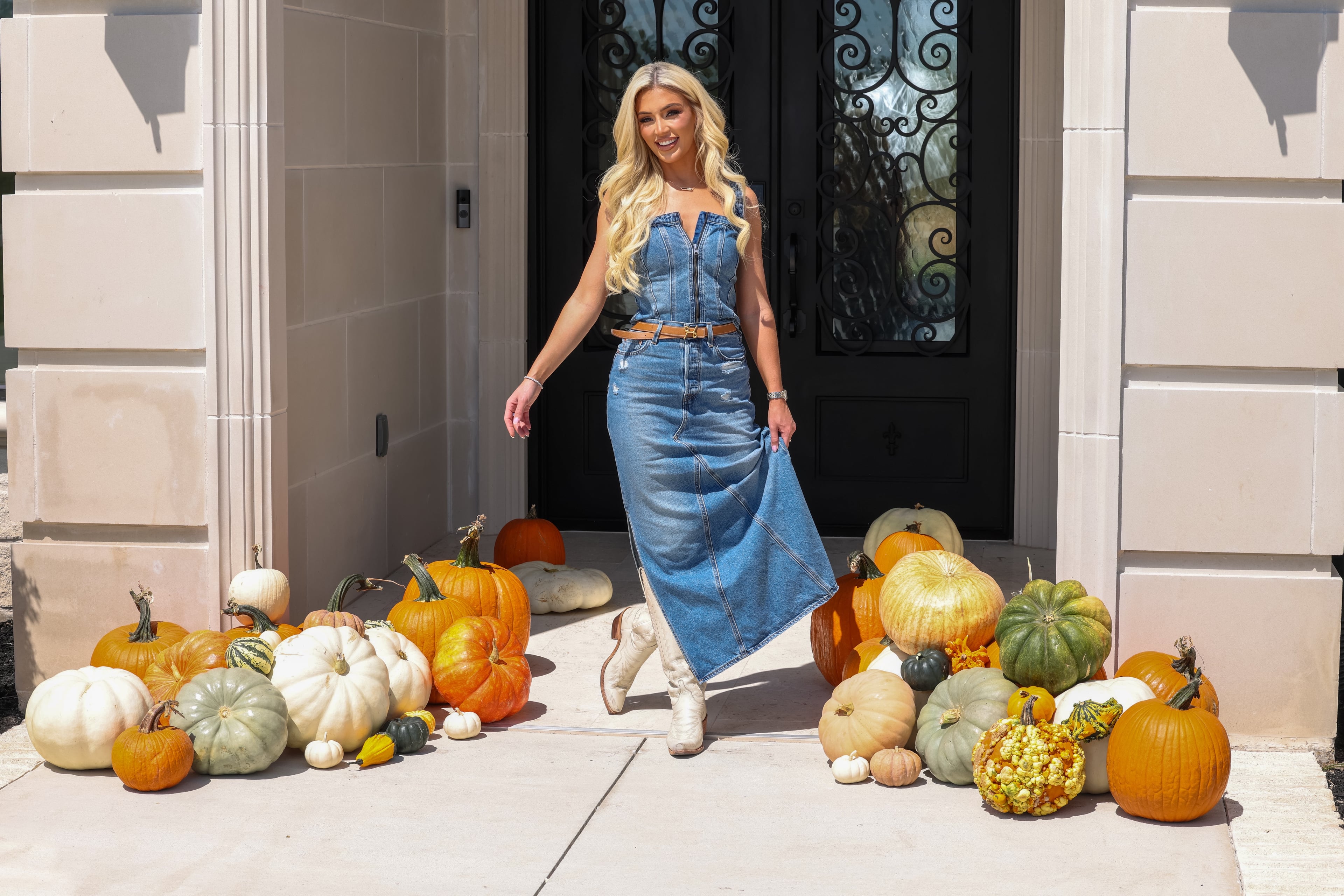 Ashley Hancock standing among orange, ivory and sage pumpkins on a front porch